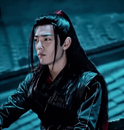 A Young Man With Long Black Hair Is Wearing A Black Jacket And A Red Ponytail . GIF