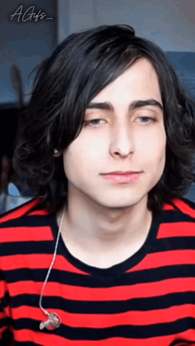 a young man with long black hair is wearing a red and black striped shirt and ear buds .