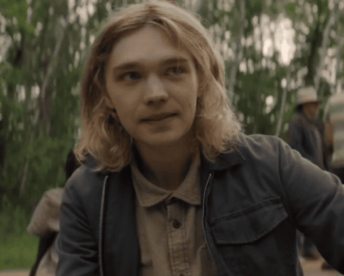 A Young Man With Long Blonde Hair Is Wearing A Denim Jacket GIF