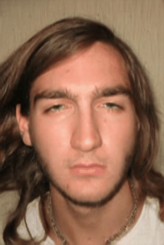 A Young Man With Long Hair And A Necklace Around His Neck Looks At The Camera GIF