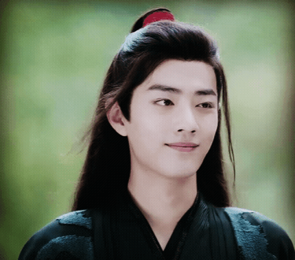 A Young Man With Long Hair And A Red Ponytail Is Smiling GIF