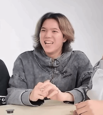 A Young Man With Long Hair Is Sitting At A Table Laughing . GIF