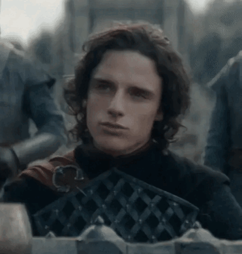 A Young Man With Long Hair Is Standing In Front Of A Fence Holding A Sword . GIF
