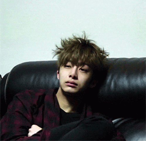 A Young Man With Messy Hair Is Sitting On A Black Couch GIF