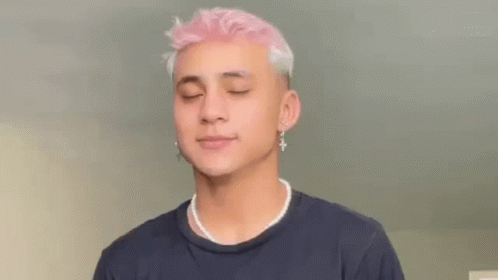A Young Man With Pink Hair And Pearl Necklace Is Wearing A Black Shirt And Earrings . GIF