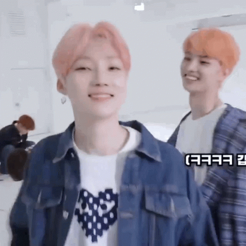 A Young Man With Pink Hair Is Smiling While Standing Next To Another Young Man With Orange Hair . GIF