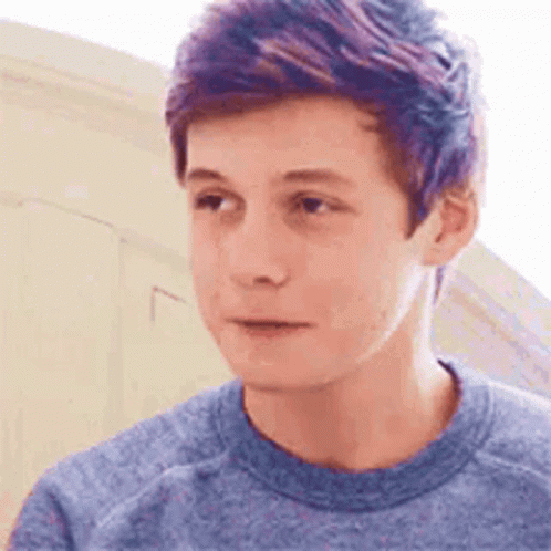 A Young Man With Purple Hair Is Wearing A Blue Shirt And Looking At The Camera . GIF