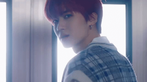 A Young Man With Red Hair And A Plaid Vest Is Standing In Front Of A Window . GIF