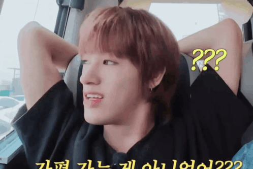 A Young Man With Red Hair Is Sitting In A Car With His Hands Behind His Head And A Question Mark On His Face GIF