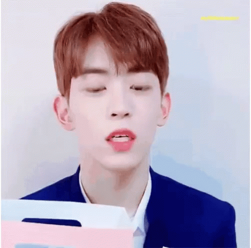 A Young Man With Red Hair Is Smiling While Holding A Pink And Blue Folder . GIF