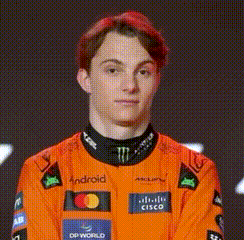 A Young Man With Red Hair Is Wearing An Orange Racing Suit And Looking At The Camera . GIF