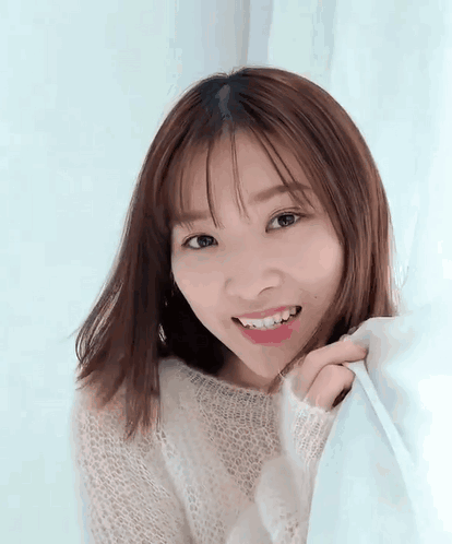 A Young Woman In A White Sweater Is Smiling While Holding A Blue Curtain . GIF