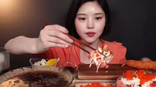 A Young Woman Is Eating Sushi With Chopsticks GIF