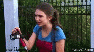 A Young Woman Is Holding A Hose In Her Hand While Standing In Front Of A Fence . GIF