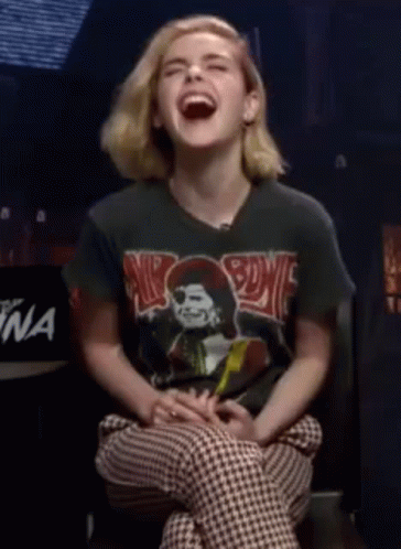 A Young Woman Is Laughing While Wearing A Black Shirt With A Picture Of A Skull On It . GIF