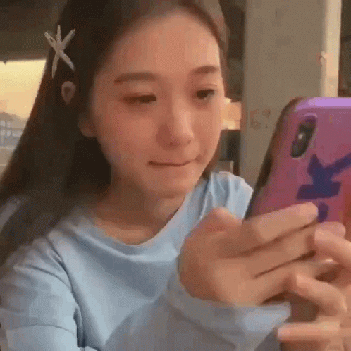 A Young Woman Is Looking At Her Cell Phone While Wearing A Blue Shirt . GIF