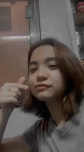 A Young Woman Is Making A Funny Face And Giving A Thumbs Up Sign . GIF