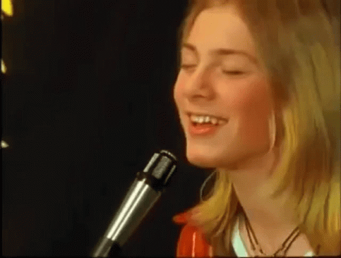 a young woman is singing into a microphone with her eyes closed .