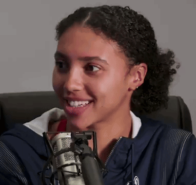 A Young Woman Is Smiling In Front Of A Microphone GIF