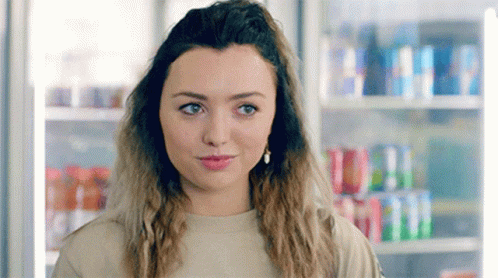 A Young Woman Is Standing In Front Of A Vending Machine Filled With Sodas . GIF