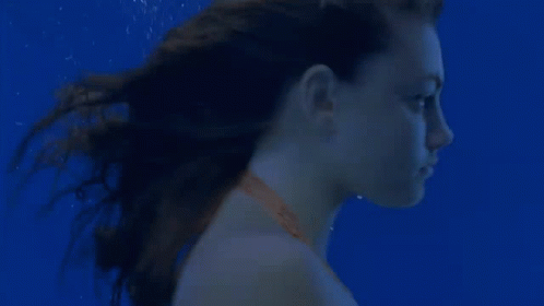 a young woman is swimming underwater in a pool .