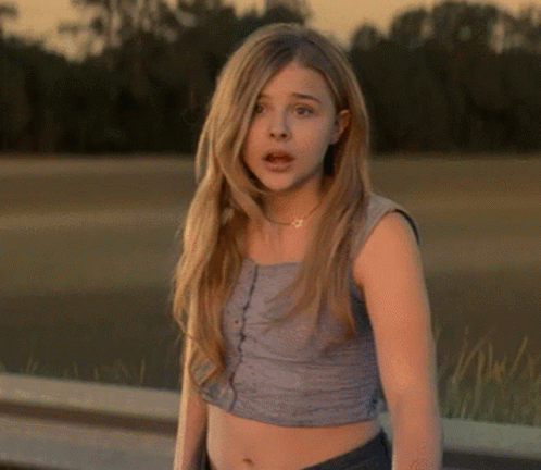 A Young Woman Wearing A Crop Top Stands In Front Of A Body Of Water GIF