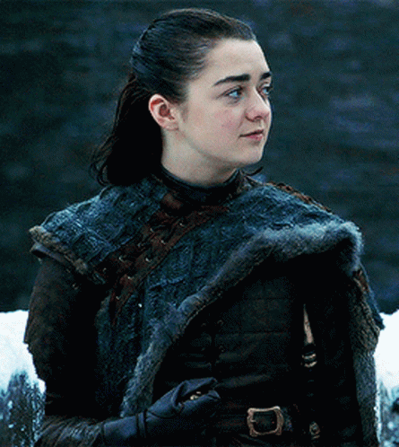 A Young Woman Wearing A Fur Coat And Gloves Is Standing In Front Of A Waterfall . GIF