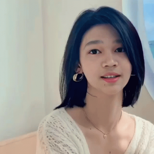 A Young Woman Wearing A Necklace And Earrings Is Smiling GIF