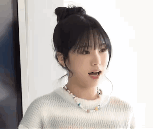 A Young Woman Wearing A White Sweater And A Necklace Is Making A Surprised Face . GIF