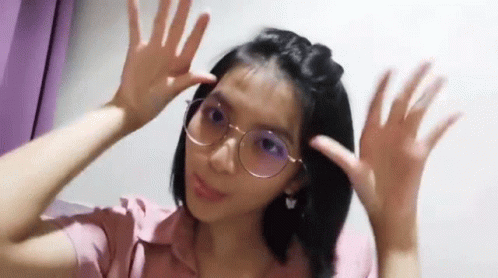 A Young Woman Wearing Glasses And A Pink Shirt Is Making A Funny Face . GIF
