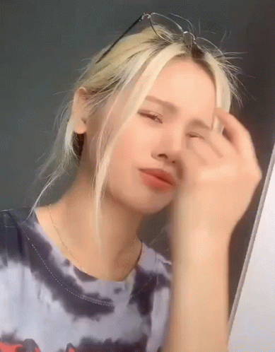 A Young Woman Wearing Glasses And A Tie Dye Shirt Is Looking At Herself In The Mirror . GIF