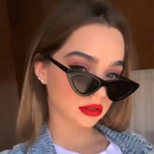 a young woman wearing sunglasses and red lipstick is looking at the camera .