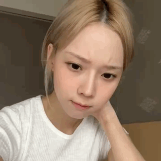 A Young Woman With Blonde Hair Is Wearing A White T-Shirt And Looking At The Camera . GIF
