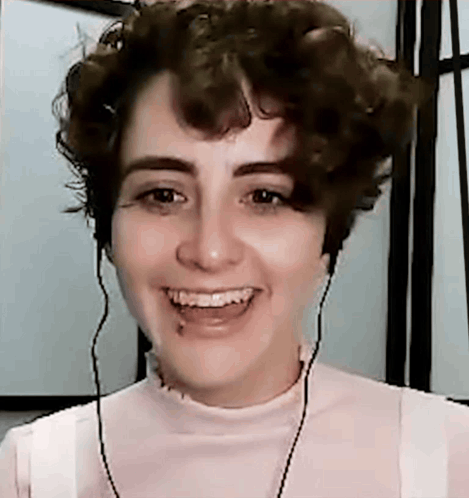 A Young Woman With Curly Hair Is Smiling And Wearing Headphones . GIF
