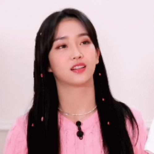 A Young Woman With Long Black Hair Is Wearing A Pink Sweater And Necklace . GIF