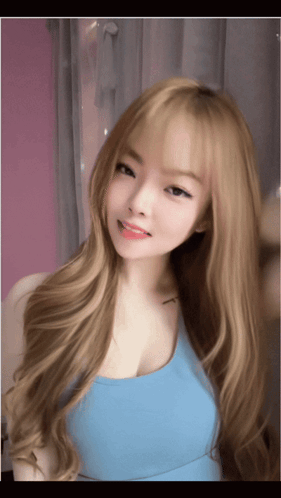 A Young Woman With Long Blonde Hair Is Wearing A Blue Tank Top GIF