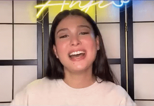 A Young Woman With Long Hair Is Smiling In Front Of A Neon Sign . GIF