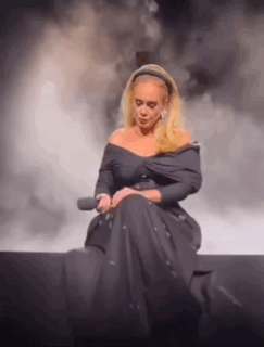 Adele Is Sitting On A Stage With A Microphone In Her Hand . GIF