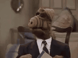 Alf From The Simpsons Is Wearing A Suit And Tie And Holding A Book In His Hand . GIF