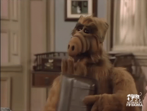 Alf From The Sitcom Sits In A Chair Holding A Briefcase GIF