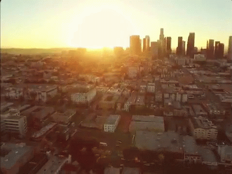 An Aerial View Of A City At Sunset With The Sun Shining Through The Clouds GIF