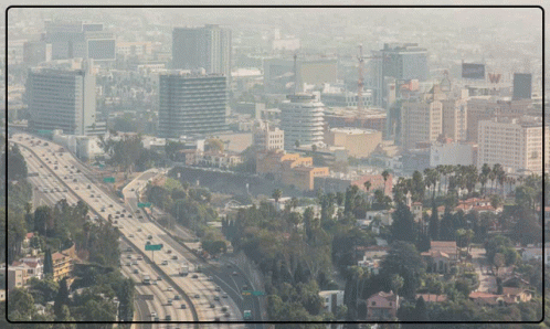 An Aerial View Of A City With A Highway In The Foreground And A Few Buildings In The Background GIF