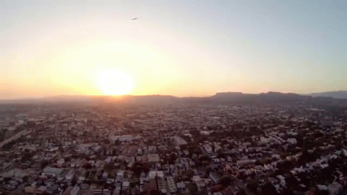 An Aerial View Of A City With The Sun Setting In The Background GIF