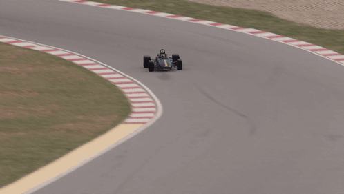 An Aerial View Of A Race Car On A Track With A Fence Behind It GIF