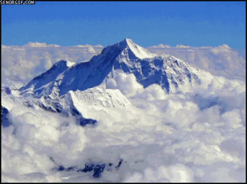 An Aerial View Of A Snowy Mountain Covered In Clouds With Senorgif.com In The Upper Right Corner GIF