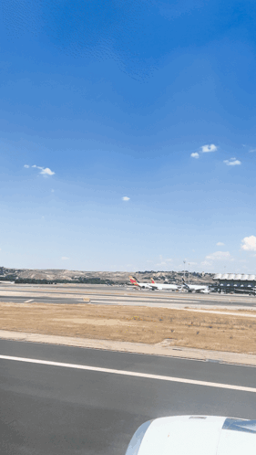 An Airport Runway With Planes Parked On It And A Blue Sky GIF