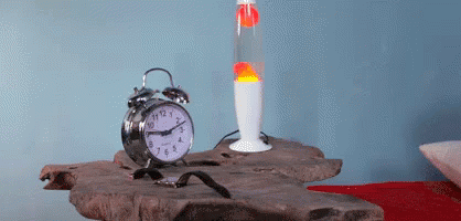 An Alarm Clock Sits On A Table Next To A Lava Lamp And A Watch GIF
