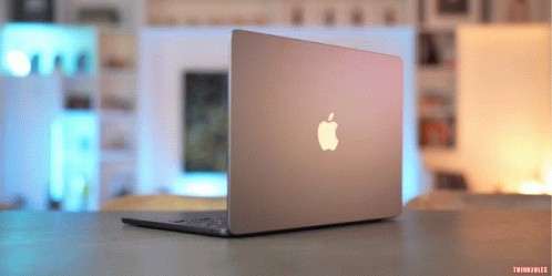 An Apple Laptop Is Sitting On A Table With A Blurred Background GIF