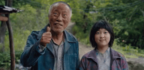 An Elderly Man And A Young Girl Are Standing Next To Each Other . The Man Is Giving A Thumbs Up Sign . GIF