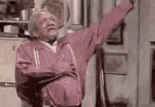 An Elderly Man In A Pink Jacket Is Dancing In A Kitchen With His Arms Outstretched . GIF